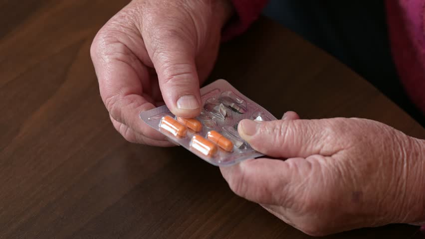 Granny prepares to take her medicine at home during the day. An elderly woman carefully removes a pill from its blister pack to take her medication at home