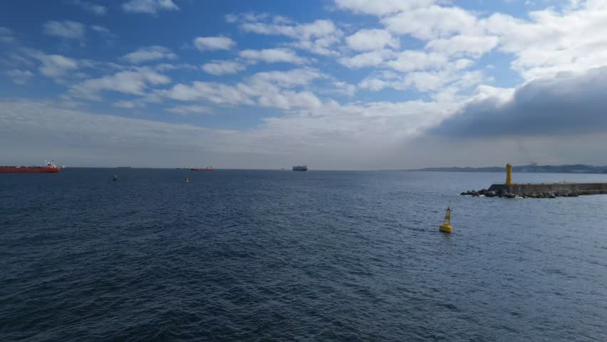 Expansive ocean scene featuring cargo ships on the horizon under a partly cloudy blue sky. This wide-angle shot is perfect for showcasing global trade, marine transport, or the beauty of the sea.