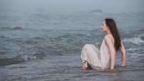 Young woman with long brown hair sits in shallow baltic sea water surrounded by fog. Calm, misty environment highlights peaceful moment at shoreline during gentle waves - Powered by Shutterstock - Get 15% off with code: PIKWIZARD15