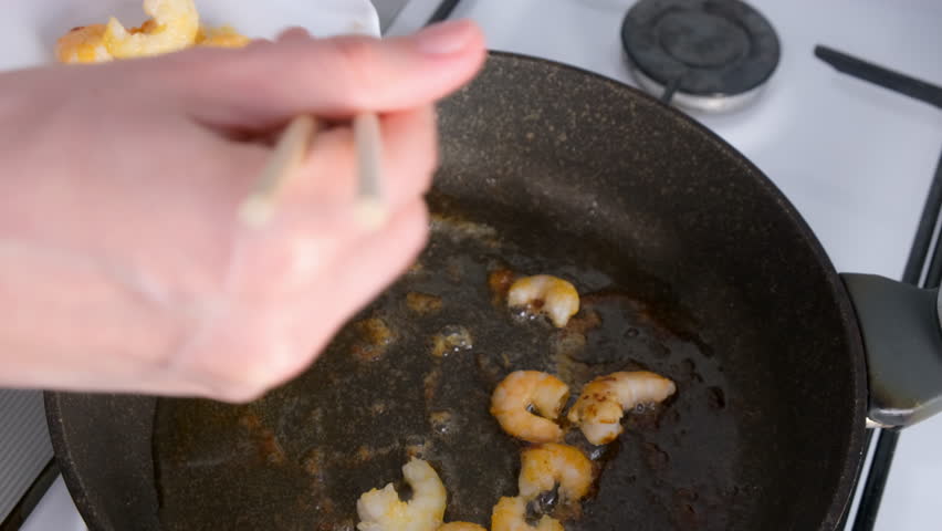Woman chef hands cooking adding shrimps from frying pan with chopsticks. Seafood dish cooking. Preparing fresh food, domestic homemade recipe. Culinary, cuisine, frying shrimp.
