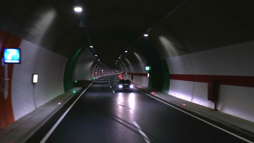 A cinematic view of driving through a modern highway tunnel. The illuminated tunnel, car headlights, and road markings highlight the dynamic atmosphere of urban transportation