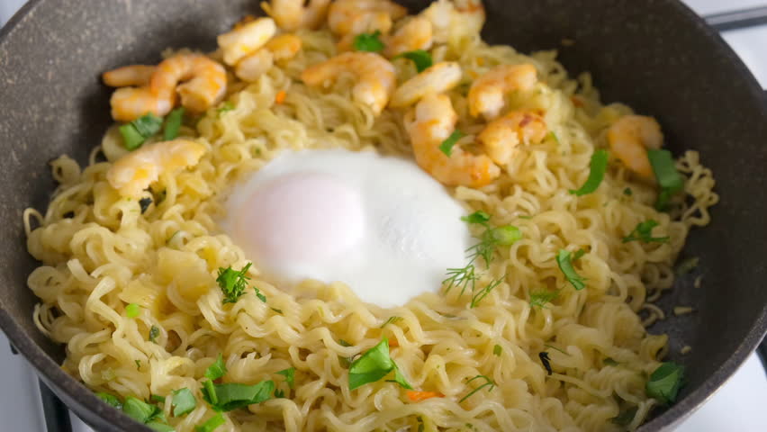 Cooking instant noodles with egg, shrimps and greenery in frying pan. Preparing Asian dish. Cook fresh food domestic homemade recipe. Culinary, cuisine, fry noodles.