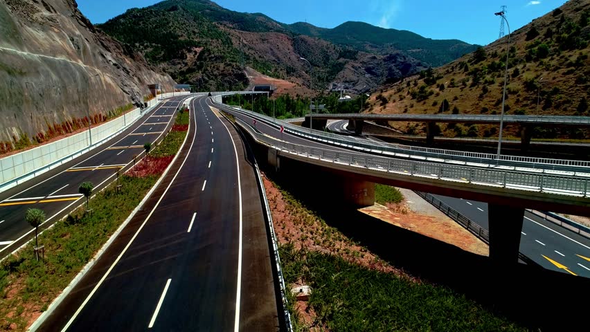 Aerial view of a modern highway interchange in a mountainous area. Featuring elevated viaducts, multi-lane roads, and advanced infrastructure reflecting modern transportation design.