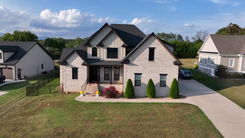 Aerial approaching shot of modern suburban house in Virginia, USA, with light brick exterior, dark roof and landscaped front yard. Luxury house with well-kept front yard in summer.