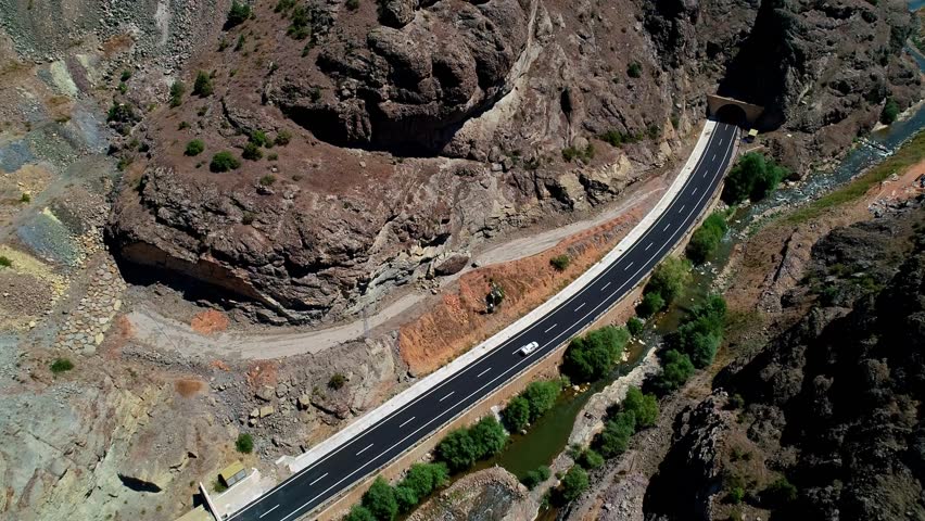Modern asphalt road and tunnel entrance passing through rocky mountains, with a river flowing alongside. A striking blend of engineering and natural landscape.