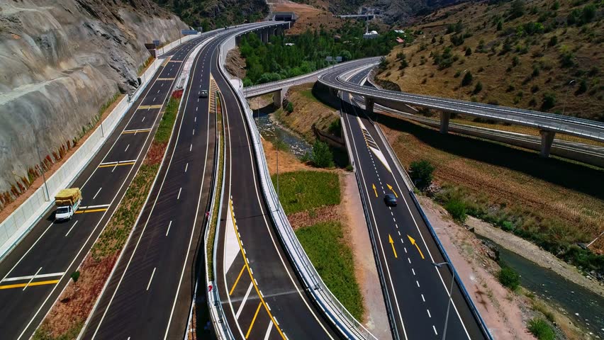 Aerial footage of a modern highway viaduct and tunnel entrance stretching through a mountainous region. Multi-lane roads showcase advanced infrastructure blending with nature.