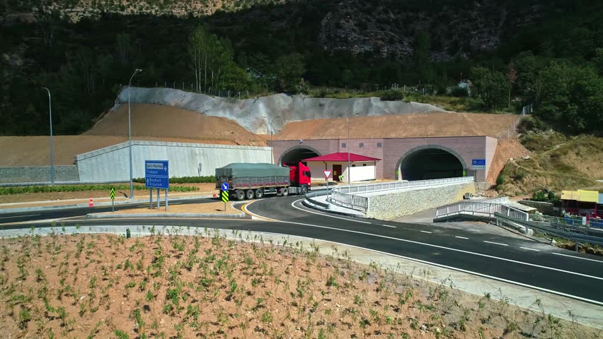 Aerial view of dual highway tunnel entrances, asphalt roads, and surrounding landscape design in a mountainous region. Modern infrastructure blending with nature.