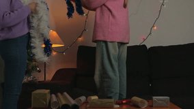 Two cheerful young women happily decorating living room wall with colorful tinsel and festive fairy lights, preparing home for christmas celebrations and creating cozy holiday atmosphere - Powered by Shutterstock - Get 15% off with code: PIKWIZARD15