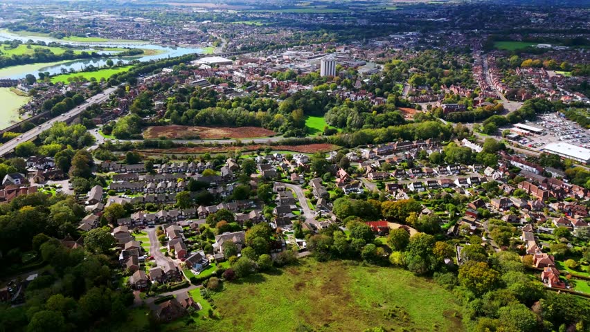 Aerial drone flies over Fareham, England, capturing trees, river, roads, and suburban houses surrounded by autumn colours glowing warmly in golden sunset light across the scenic landscape.