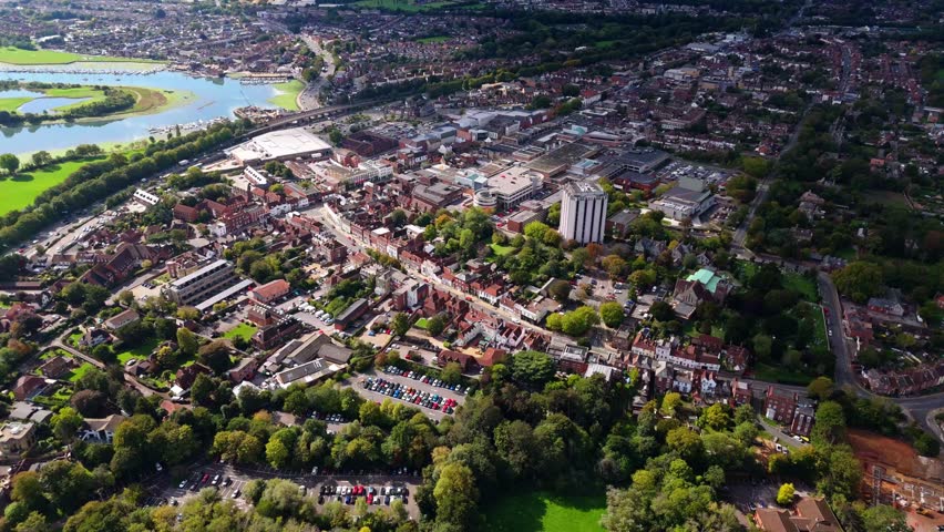 Aerial drone pans left over Fareham town centre with river and trees, capturing roads, cars, and autumn colours glowing warmly in golden sunset light across the scenic English landscape.
