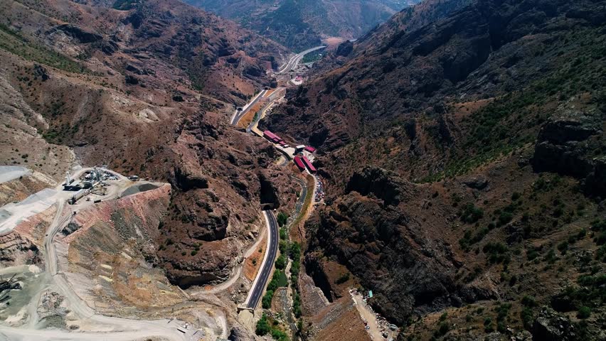 Aerial footage of a modern highway interchange with tunnels, bridges, and viaducts in a mountainous region. Advanced transportation infrastructure reflects engineering excellence.