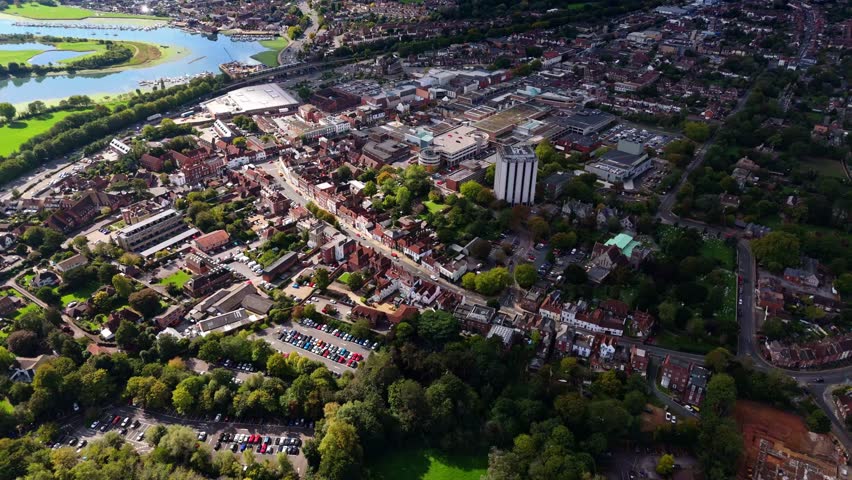 Aerial drone pans left over Fareham town centre with river and trees, showcasing cars, roads, and autumn colours glowing warmly in golden sunset light across the scenic English countryside.