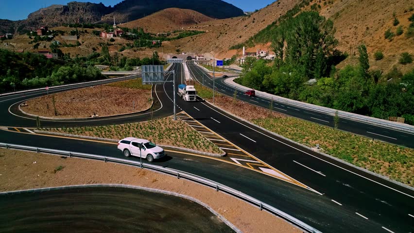 Aerial view of a modern highway interchange in a mountainous region. Multi-lane roads and curves highlight advanced engineering and the development of transportation infrastructure.