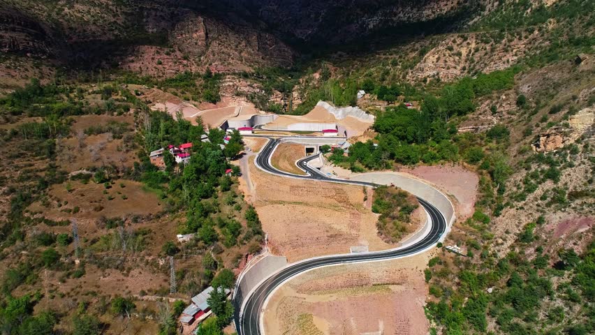 Aerial footage of winding highways and tunnels under construction in a mountainous region. Infrastructure development reflects modern transportation blending with nature.