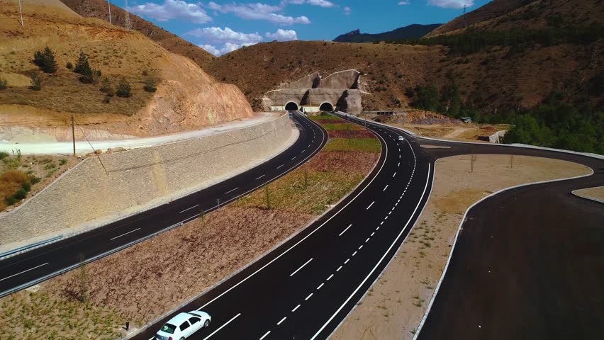 Aerial view of a modern highway interchange in a mountainous region. Multi-lane roads and curves highlight advanced engineering and the development of transportation infrastructure.