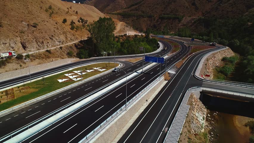 Aerial view of a modern highway interchange in a mountainous region. Multi-lane roads and curves highlight advanced engineering and the development of transportation infrastructure.