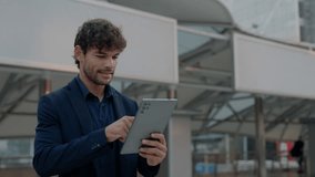 Portrait of Hispanic man investor makes deal online via tablet and smiles against office building. Male Latin trader controls transactions on portable device in downtown block - Powered by Shutterstock - Get 15% off with code: PIKWIZARD15