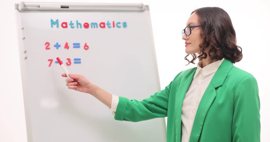 Woman teacher stands at whiteboard and explains simple math examples against white background. Female explains easy arithmetic problems. Slow motion