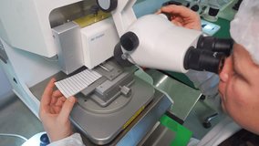 Research lab researcher holds an LED board, examines it through a microscope, and checks for quality and manufacturing defects. A quality assurance employee in a white coat and cap at his workstation. - Powered by Shutterstock - Get 15% off with code: PIKWIZARD15
