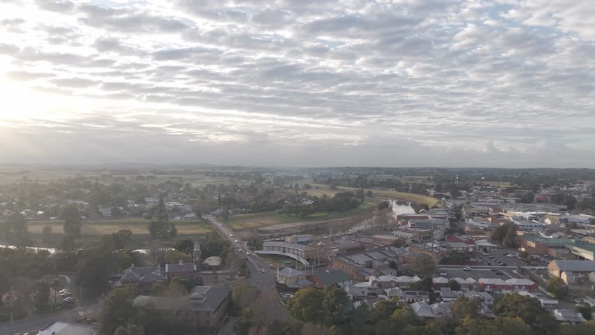 Drone rises at dawn revealing misty Maitland town and Hunter River, soft golden sunrise glow, panoramic aerial establish, NSW Australia