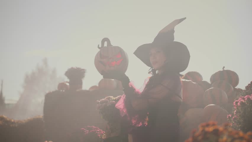 unrecognizable dark silhouette beauty young woman witch with orange pumpkin carved Jack o Lantern in foge smoke. fantasy girl, dress black hat. Halloween holiday harvest pumpkins Thanksgiving Day 4k.