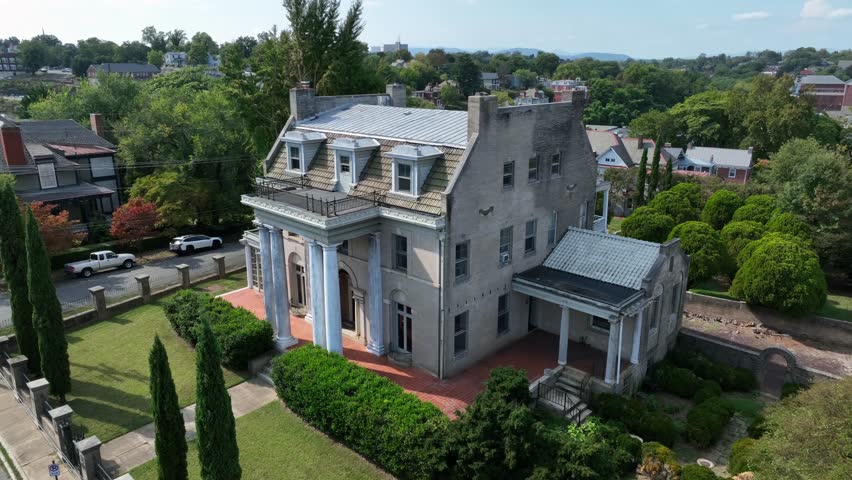 Historic American house with classical columns, surrounded by trees and residential streets, blending old architecture with a quiet neighborhood atmosphere. Aerial view. Sunny summer day in Lynchburg.
