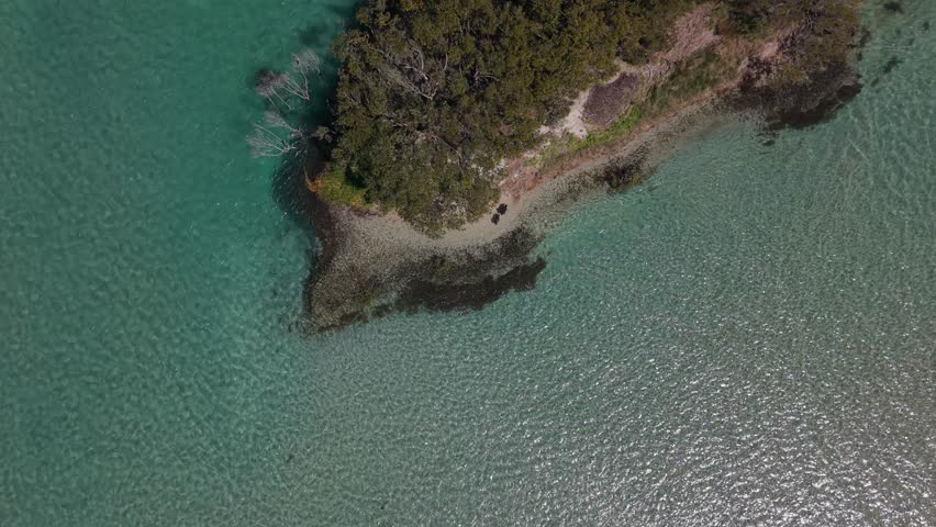 Calm turquoise sea flows around island point, aerial pullback reveals tropical oasis, Swansea Pirrita Island New South Wales