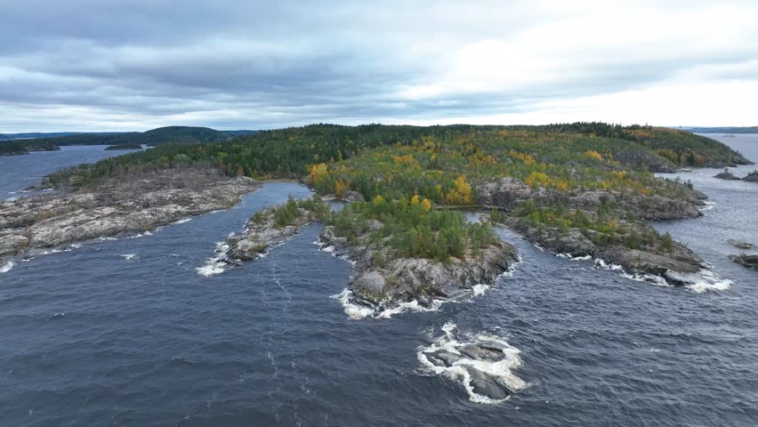 A high angle aerial view of a wide, powerful river with rapids and white water flowing around exposed granite rock formations, surrounded by pine forest and yellow autumn foliage