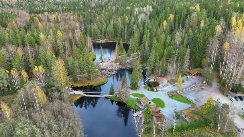 Ruskeala, Russia - September 13, 2024: A high angle aerial view of a dark, winding river system connecting small lakes with rapids, surrounded by dense autumn forest and showing wooden tourist facilit