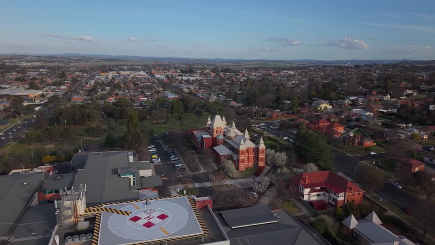Wide aerial establishing above Bathurst residential streets and hospital with golden sunset light and long shadows, NSW Australia