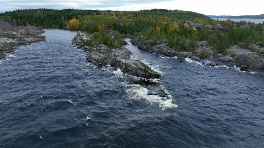 A high angle aerial view of a wide, powerful river with rapids and white water flowing around exposed granite rock formations, surrounded by pine forest and yellow autumn foliage