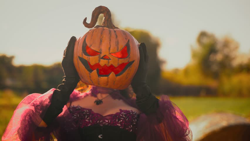 Art video real person woman with orange pumpkin for a head carved Jack o Lantern. fantasy happy smiling evil face, mystery girl, purple dress. Halloween holiday harvest lots pumpkins Thanksgiving Day