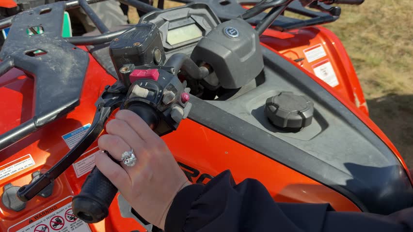 A landscape action video showing a hand controlling an ATV on a dirt trail. Sunlight flickers on an oval diamond engagement ring with platinum band as the ride accelerates.