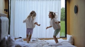 Two carefree little sisters laughing and jumping together on a comfortable bed in a bright, modern bedroom. Happy children enjoying an energetic and playful morning at home or on vacation - Powered by Shutterstock - Get 15% off with code: PIKWIZARD15