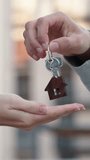 Vertical close up of hands, male real estate agent handing over house key with home shaped keychain to young woman in front of modern apartment building. Concept of real estate deal, housing service. - Powered by Shutterstock - Get 15% off with code: PIKWIZARD15