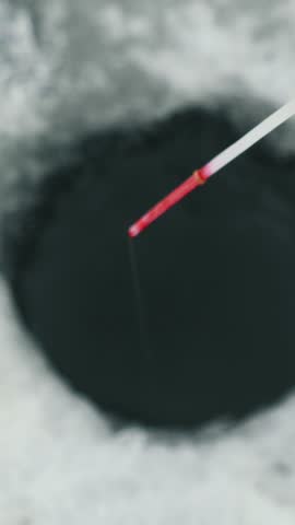 Fishing rod for winter fishing in ice hole, close up shot. Winter fishing concept. Man is catching fish in hole on frozen river. Vertical video