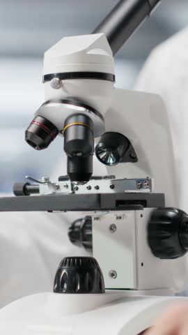 Vertical Video Male professional scientist investigates tray samples under optical microscope. Observation tool with magnifying glass highlight biochemistry and medical research, bioengineering