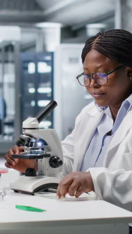 Vertical Video Researcher using microscope and specimen tray in laboratory workspace. Optical instrument, lens system and magnifying glass support clinical testing and biotechnology for healthcare