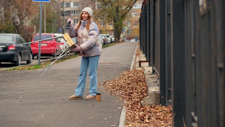 Woman is packing wooden paint box closing it after drawing a picture on plain air filmed in slow motion at cold autumn day. Cheerful lady is finishing creating a picture outdoors and going home