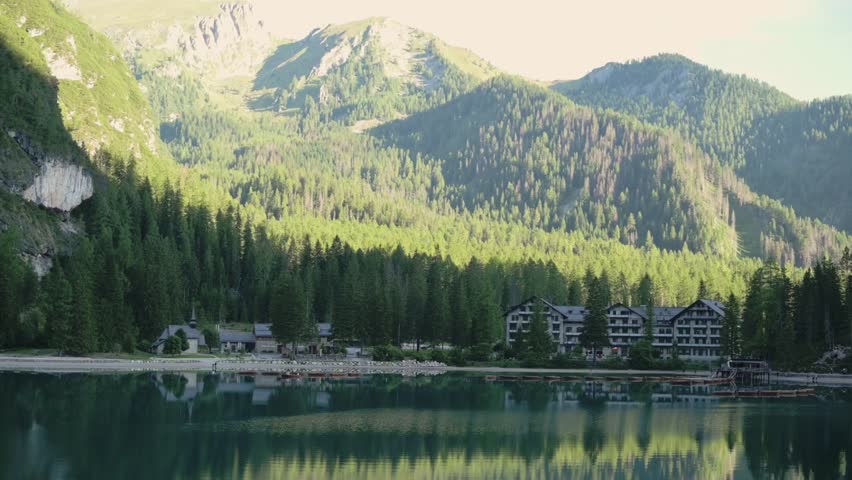 Lago di Braies with hotels and dense pine forest reflecting in calm emerald waters