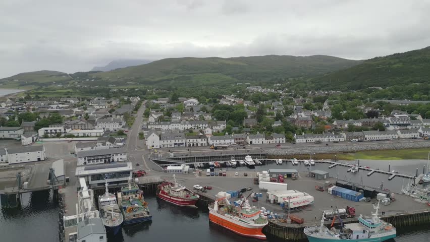 Fishing boats docked in Ullapool harbour on Loch Broom in Scottish Highlands with town and hills