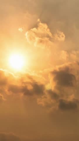 A dramatic time-lapse of a golden sunrise or sunset. The sun emerges from behind dark, moving clouds, creating a beautiful and majestic skyscape.