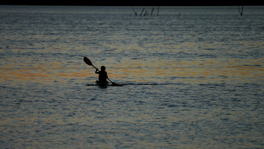 silhouette of a young kayaker paddling at dusk on a lake