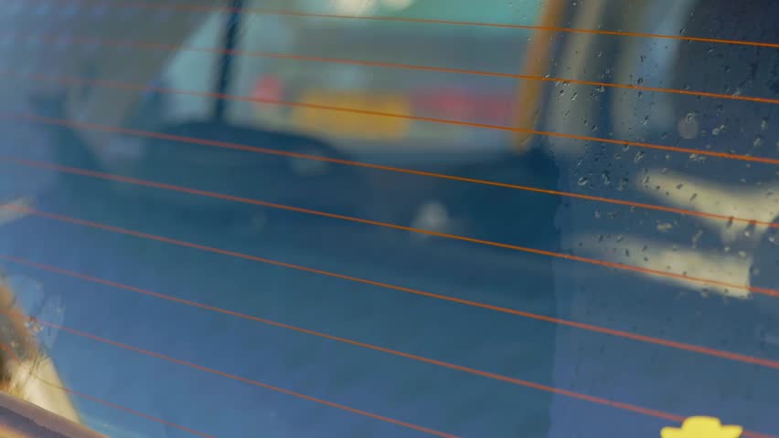 Close up washing yellow car rear window with blue mitt and lots of shampoo suds
