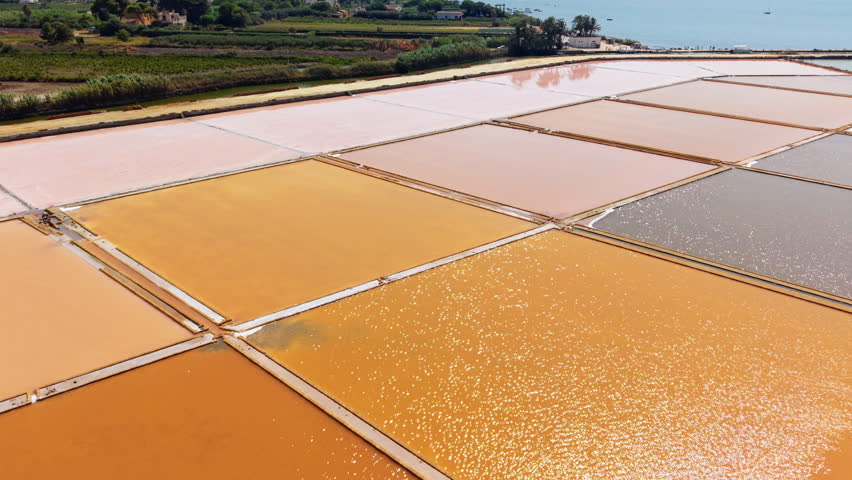 Aerial drone view of colorful salt pans in Sicily with geometric patterns and glowing water, stunning landscape view.