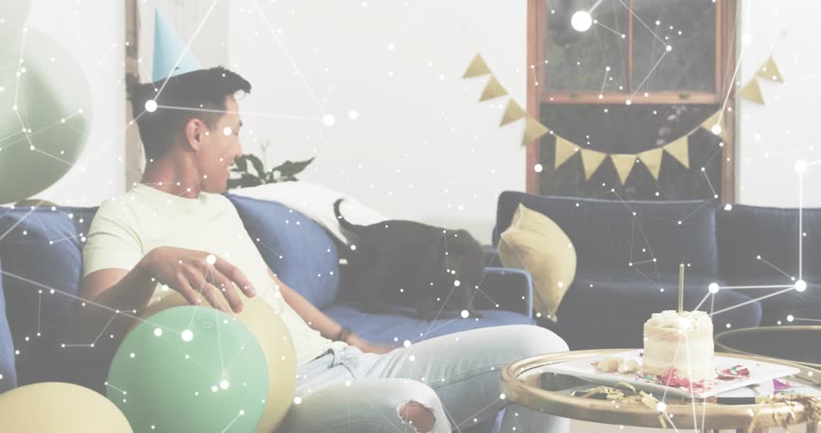 Picking up two balloons, man juggling while adjusting dog hat and offering bowl for birthday party. Festive, celebration, companionship, cheerful, playful, cozy, lifestyle