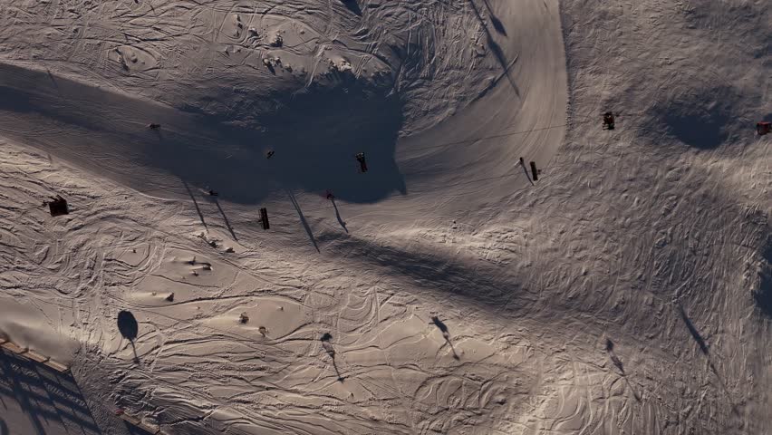 People skiing and snowboarding at Cardrona ski resort at sunrise, tracks in snow and long shadows. New Zealand. aerial top-down view