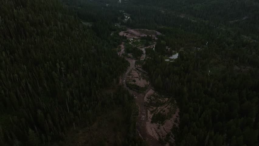 Drone dolly out tilt up shot of a valley in Uinta-Wasatch-Cache National Forest, Utah, at sunset with the Provo River surrounded by pine trees, Highway 150 to the right, mountains and a summer sky.