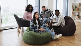 Group of diverse young adults sitting on beanbags in bright modern office posing for selfie. Relaxed and cheerful atmosphere. Ideal for concepts of teamwork, friendship, and modern workplace dynamics. - Powered by Shutterstock - Get 15% off with code: PIKWIZARD15