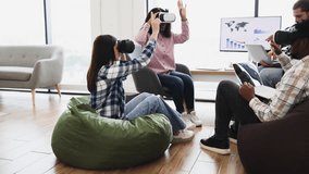 Two young women using VR headsets in modern office. One sits on bean bag others engage with technology. Mixed environment promoting innovative collaboration. - Powered by Shutterstock - Get 15% off with code: PIKWIZARD15